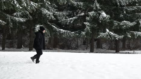 Mann-Im-Schwarzen-Wintermantel,-Der-In-Einem-Verschneiten-Winterwald-Von-Links-Nach-Rechts-Geht