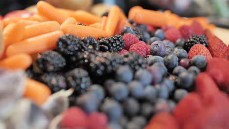 Tracking-shot-over-fruit,-berries,-and-vegetables-arranged-on-cutting-board