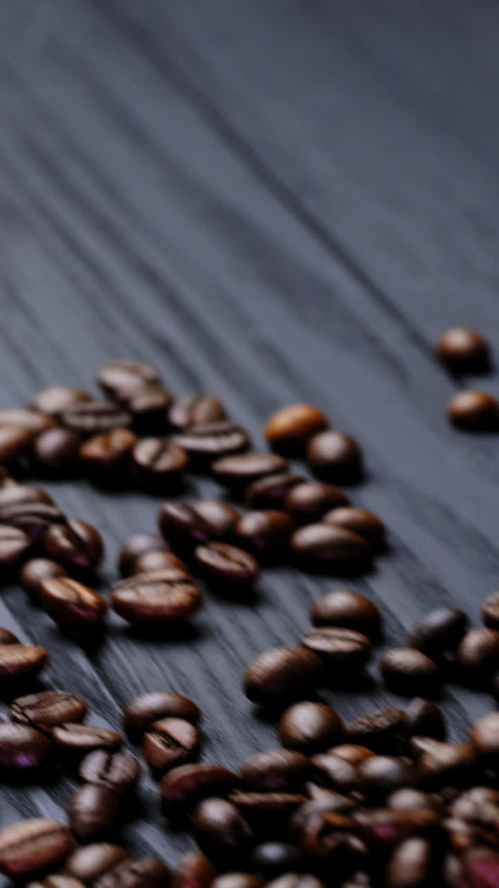 Scattered coffee beans on wooden background. Small sack on the table with roasted coffee beans lying nearby. Brown grains of coffee. Vertical video