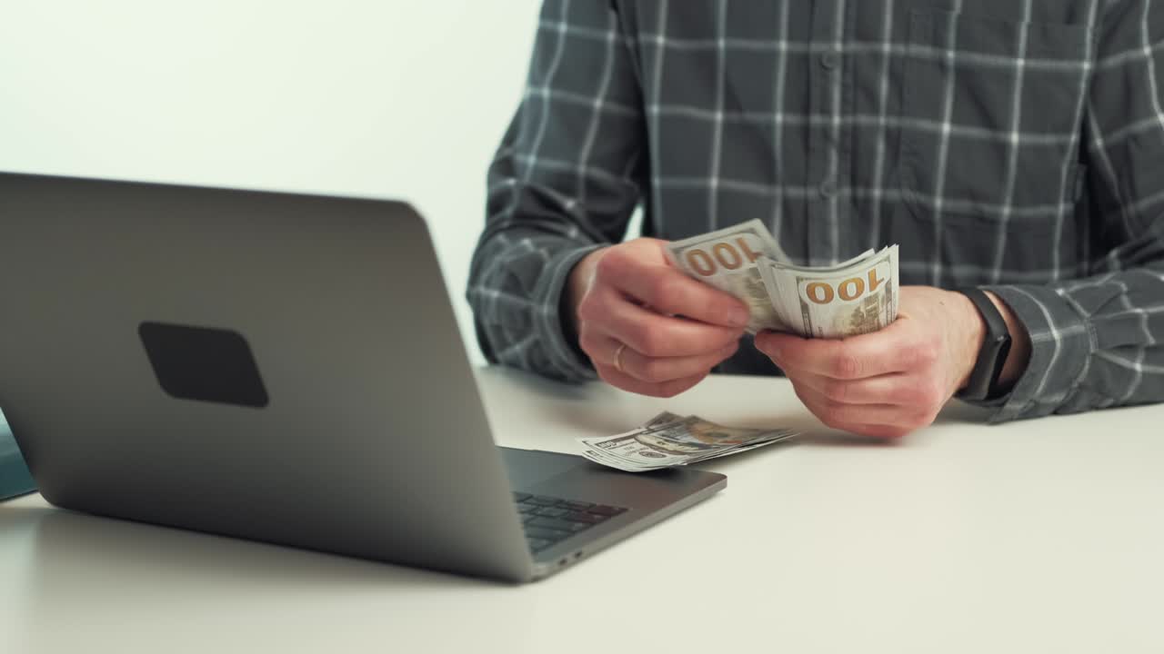 близкое видео человека, считающего деньги возле ноутбука на рабочем столе.