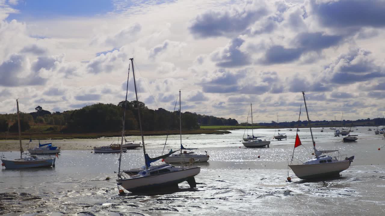Panning, handheld shot right to left looking downstream of a river at low tide showing mud and boats in the mud
