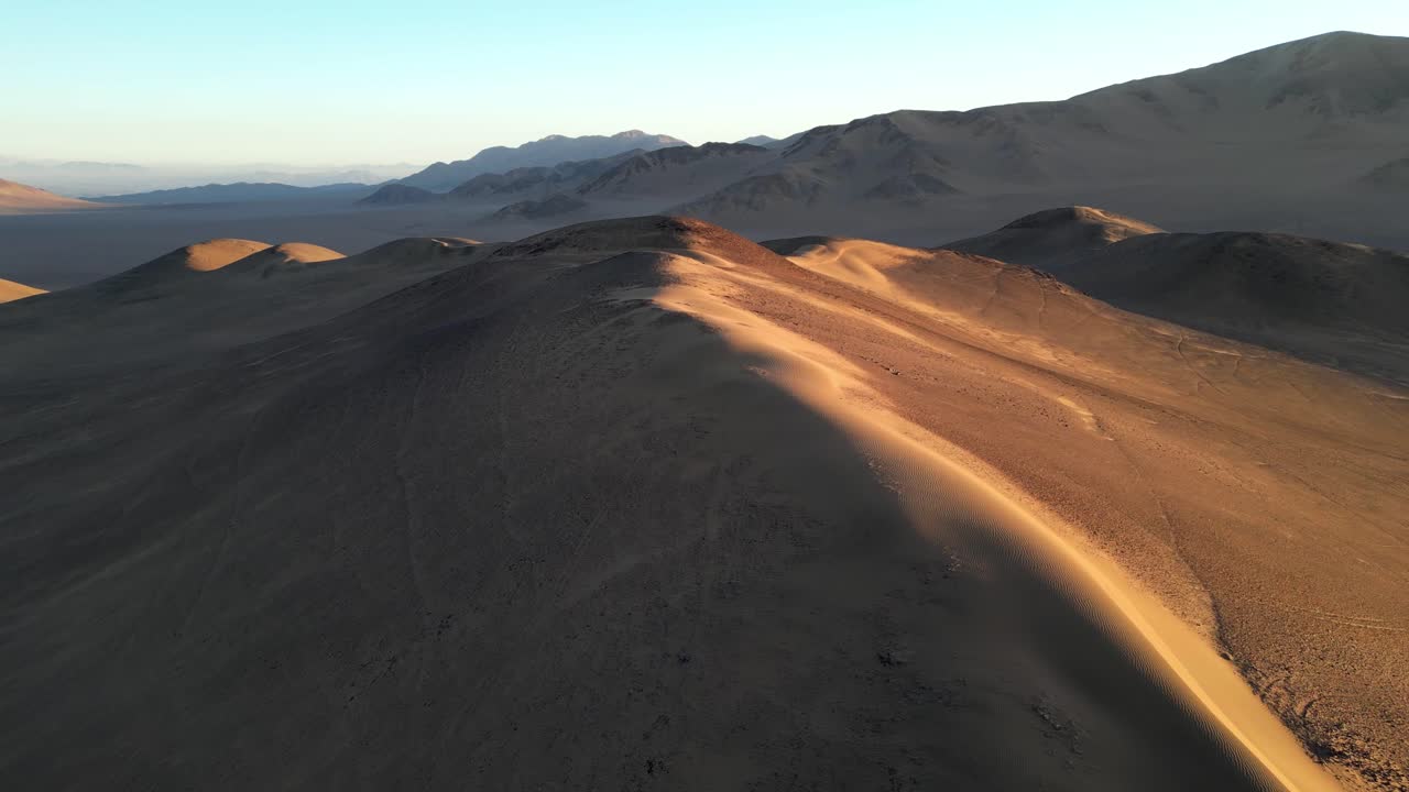 Cinematic aerial shot revealing the textured slopes of the Atacama’s legendary dune in warm evening tones