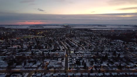 ciudad cubierta de nieve al atardecer, mostrando luces de calle brillantes y campos distantes bajo un cielo colorido
