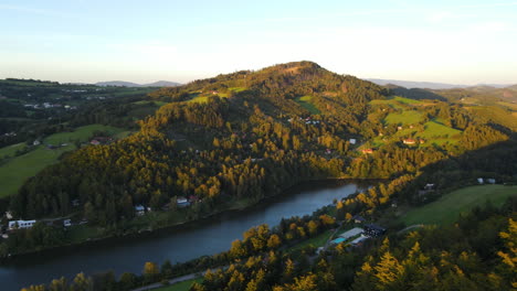 Panoramic-view-of-a-dam-in-the-middle-of-a-mountain-area-with-hills-and-forests-around-with-the-sun-in-the-background