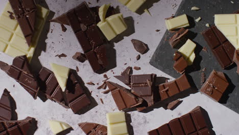 person picking up piece from broken bars of milk plain and white chocolate