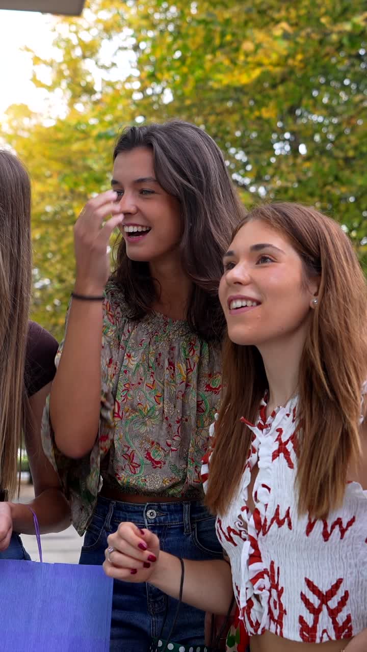 Tre giovani donne felici che camminano e parlano con borse della spesa all'aperto.