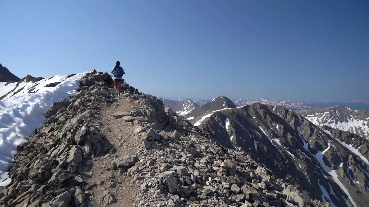 alpinista femenina en la cima de la cordillera con nieve en las laderas