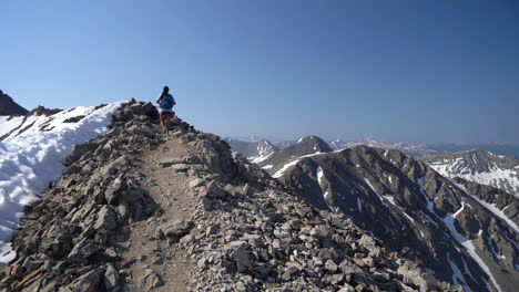 female mountaineer on top of mountain range with snow on slopes