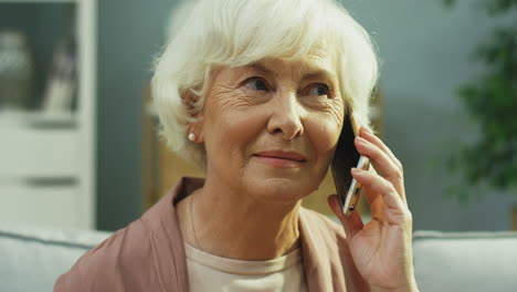 close up of the old woman talking on the mobile phone and smiling in the living room