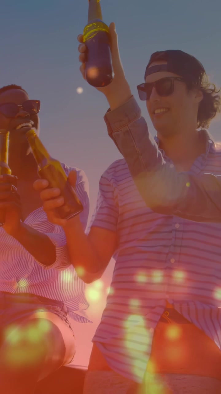 Video verticale: Amici che brindano con la birra, alzando i boccali al tramonto con sovrapposizione bokeh per il viaggio.