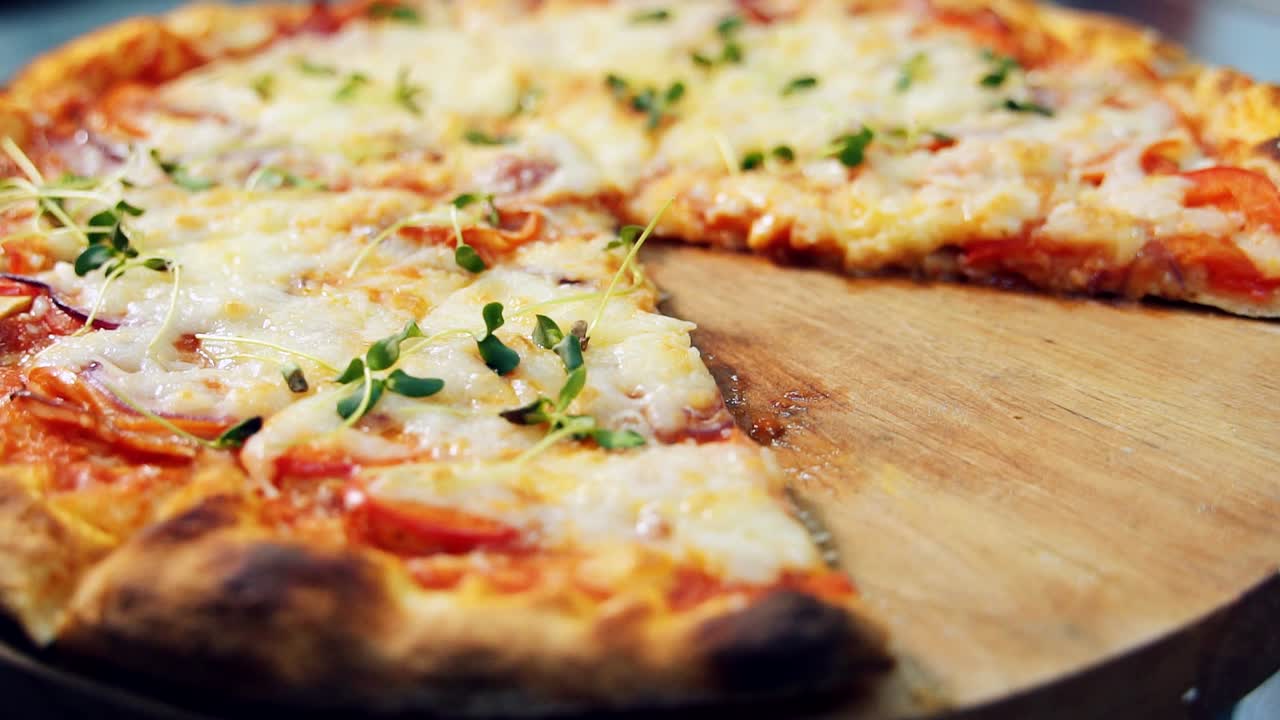 Hot Italian pizza with tomato, cheese and herbs. Rotating on wooden table. Pizza cut into slices