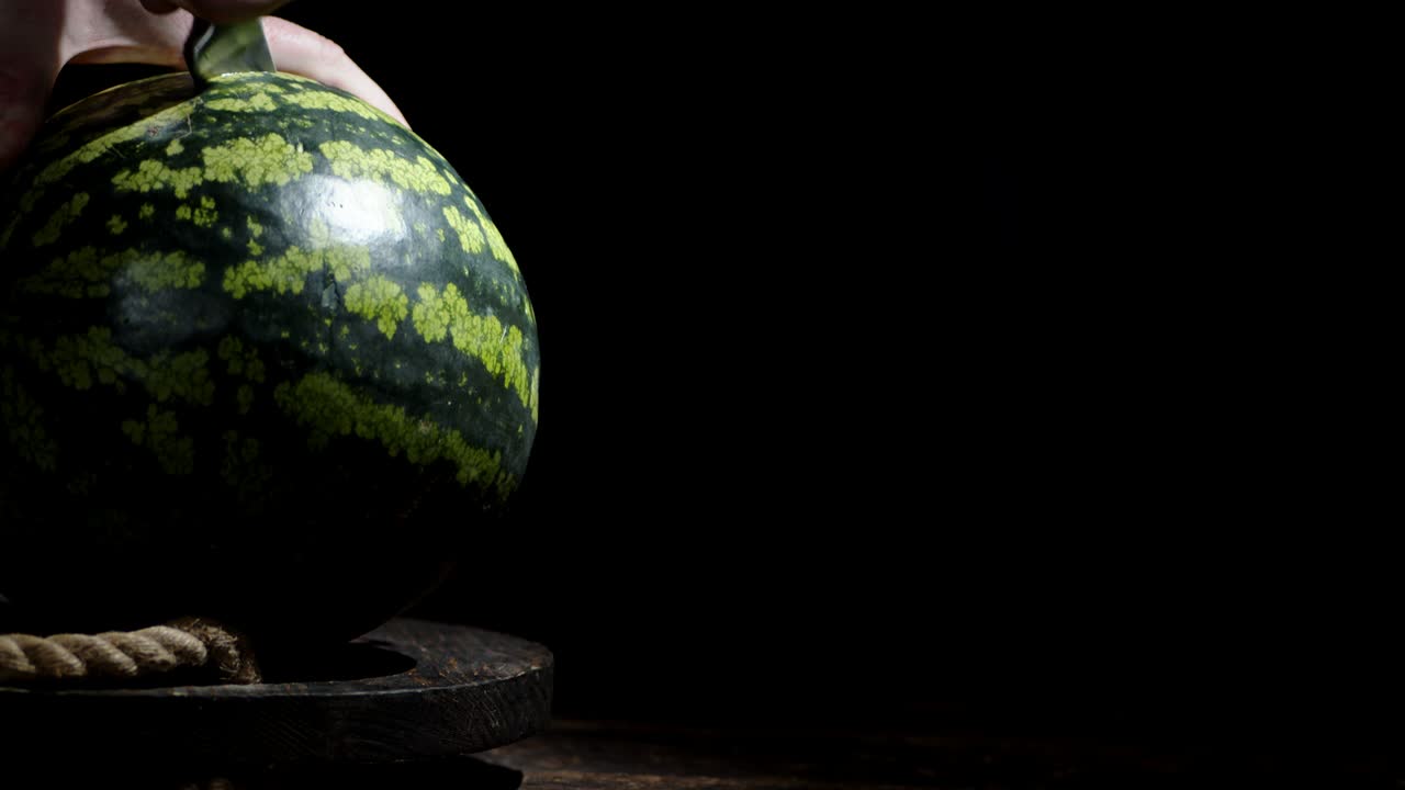 Male hand with a knife cut a watermelon into two halves.