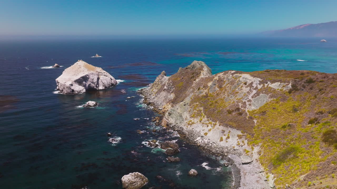 Rocks overgrown with moss surrounded by blue deep waters. Stunning seascape with hazy line of horizon on sunny day.
