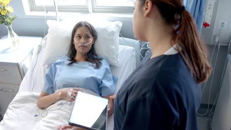 diverse female patient in hospital bed and female doctor using tablet talking, slow motion