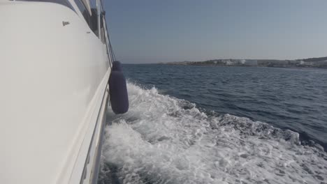 view off the side of a yacht as it speeds through mediterranean waters with the shore in the distance