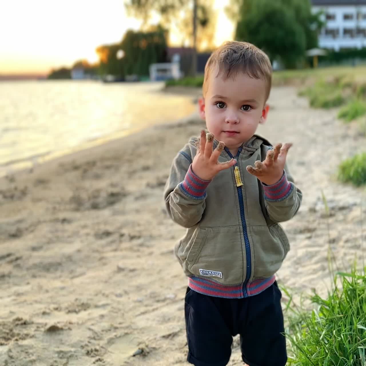 Un bellissimo bambino caucasico è in piedi sulla spiaggia e guarda le sue mani sporche di sabbia. Il bambino batte le mani per pulirle