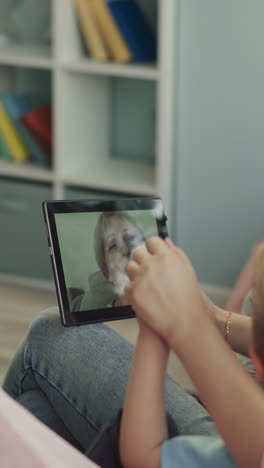 grandma talks to grandchildren and daughter on video call via tablet. woman holds modern gadget letting kids to see granny on screen closeup