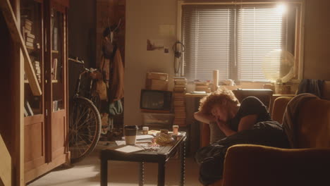 melancholic man lying on couch in cluttered room, staring at antidepressants