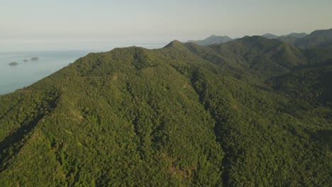 slow rotating aerial shot high above the tree covered mountains with the pacific ocean in the distance on the rainforest island of koh chang, thailand