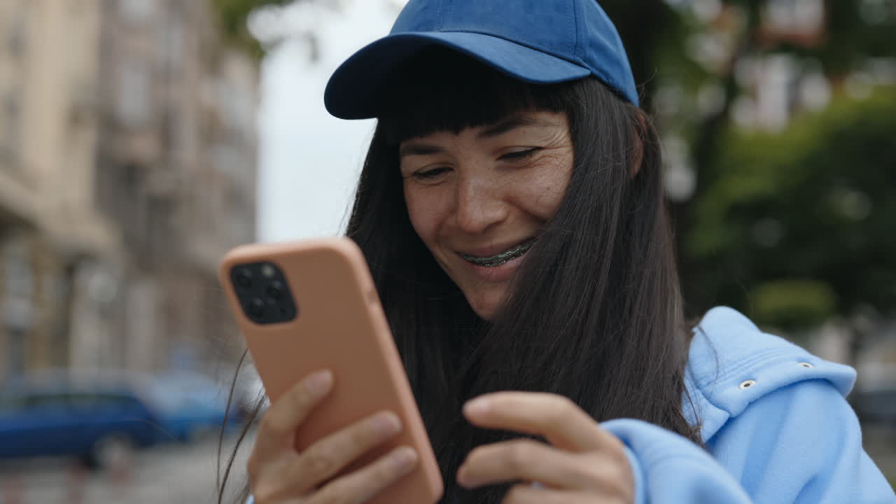 Woman with blue cap using smartphone on street