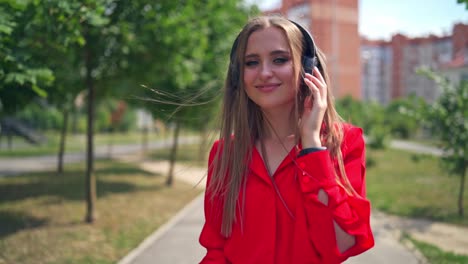 attractive woman listening to music outdoors. young female in red dress with headphones enjoys music in the city street in summer.