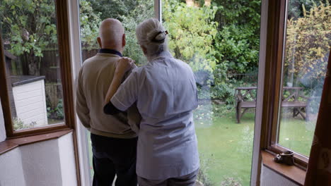 elderly couple looking out the window with caregiver