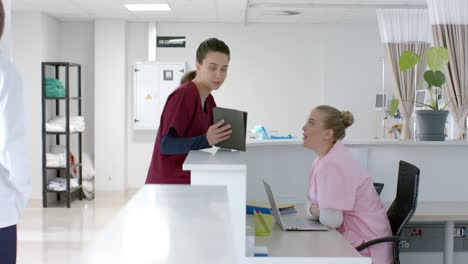 Caucasian-female-doctor-talking-to-medical-receptionist-at-front-desk-at-hospital,-slow-motion