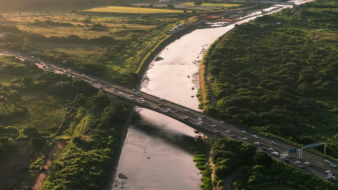 Drone clip of a busy highway as vehicles travel in both directions crossing over a river below and flora on each side creating a peaceful view