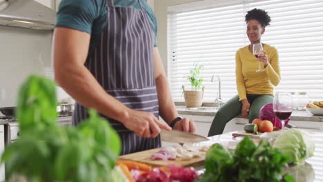 video of happy diverse couple preparing meal, drinking wine and having fun in kitchen
