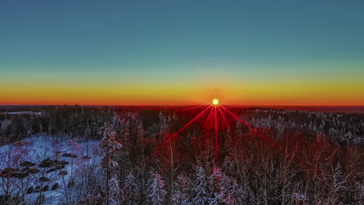 큰 숲 뒤의 겨울 일출은 태양이 높을 때 먼저 하늘을 오렌지색으로 아름다운 파란색으로 바꿉니다.