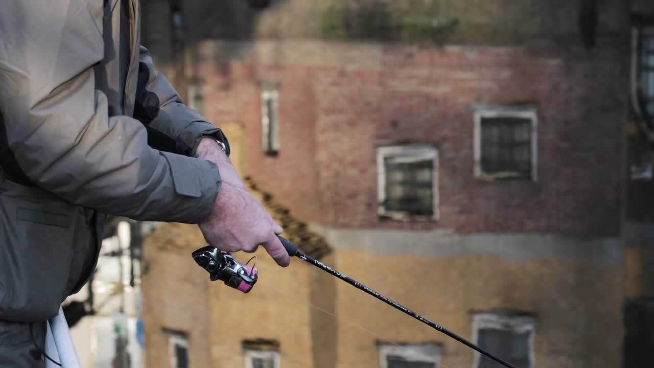 A Fisherman spinning his fishing reel in a pond with reflecting buildings in the water