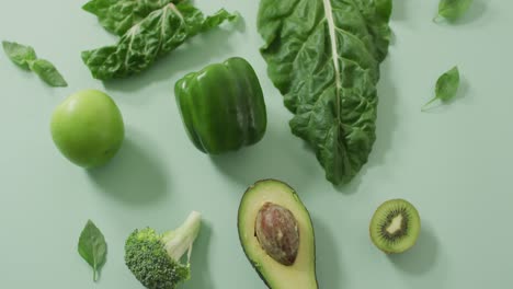 Video-of-fresh-avocado,-broccoli,-green-pepper,-apple-and-green-leaves-on-green-background
