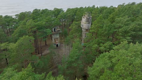Establishing-aerial-view-of-old-Soviet-military-concrete-observation-watchtower,-pine-tree-forest,-Liepaja-,-military-heritage,-Nordic-woodland,-wide-drone-shot-moving-forward,-tilt-down