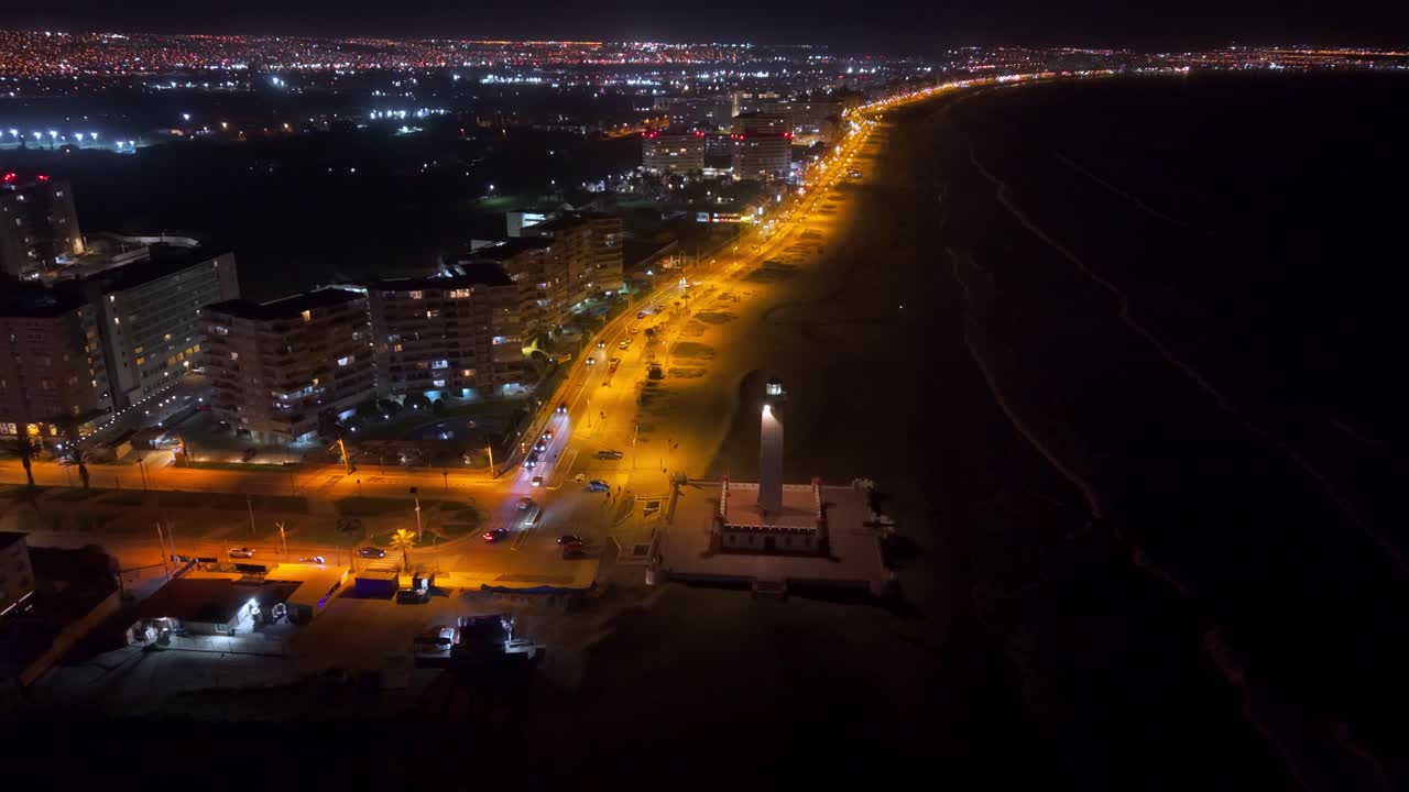 Flyover establishing shot of the waterfront of the city of La Serena with the Monumental Lighthouse at night illuminated by streetlights