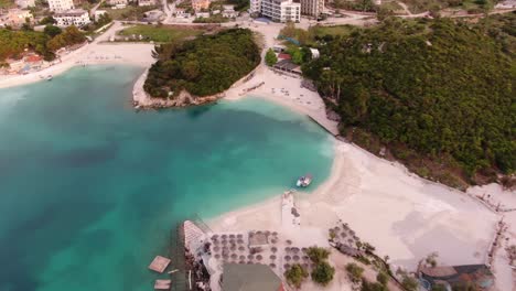 Drone-view-in-Albania-flying-over-blue-crystal-clear-water-and-white-sand-beach-on-sunset-and-hotels-in-Ksamil