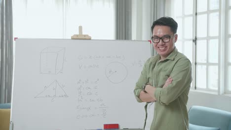 asian male teacher with glasses crossing arms and smiling to camera while teaching math at home