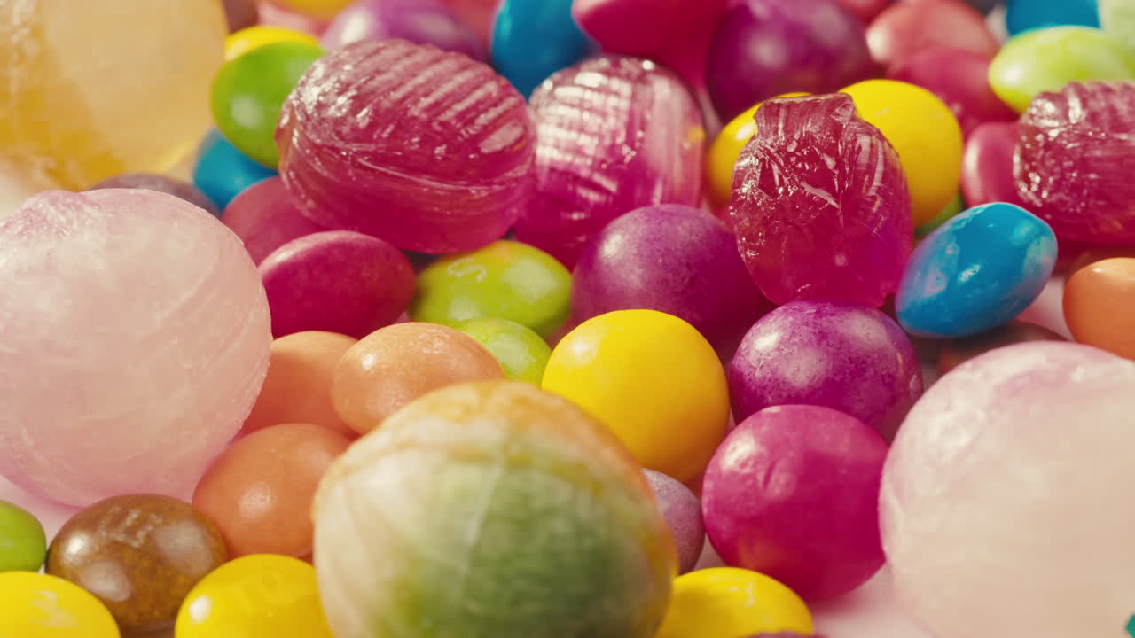 Colorful dragee candies, lollipops, bonbons on white background, move in circle, side view close-up. Summer bright texture studio shot for store, supermarket. Mix of children's sweets made of sugar.