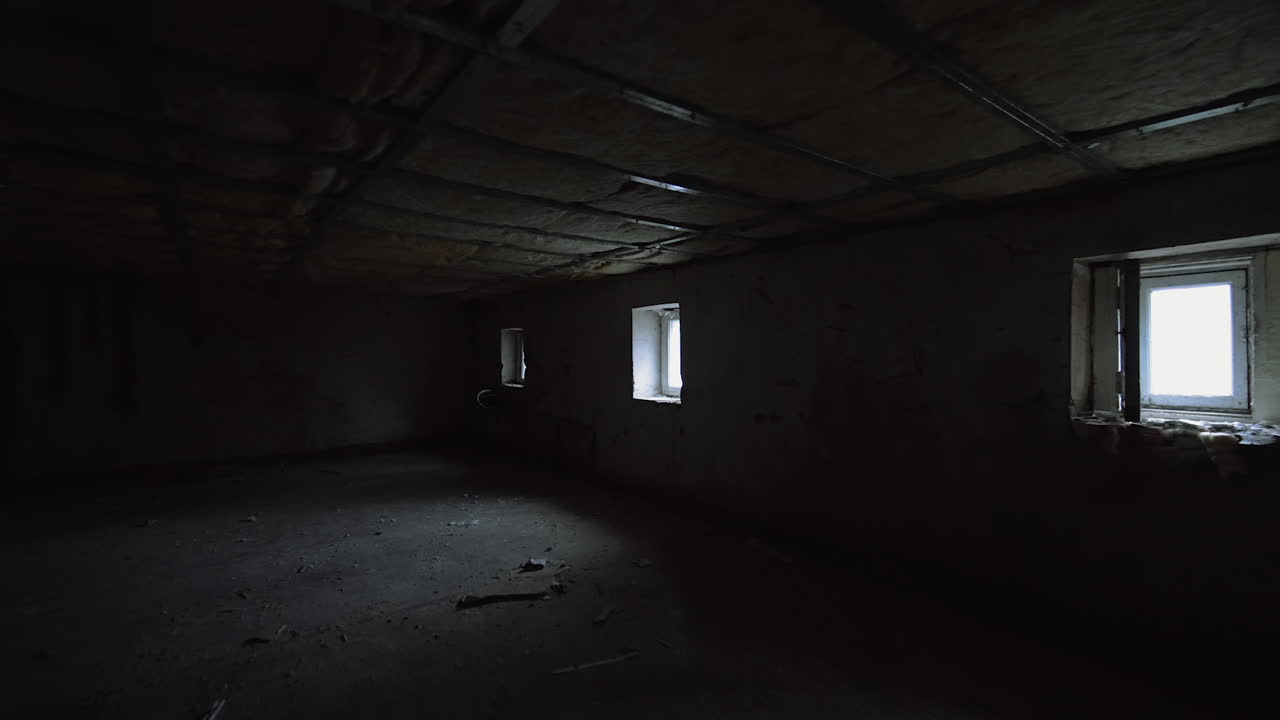 Big dark room with low ceiling and little windows. Dirty premise interior with light coming from windows.