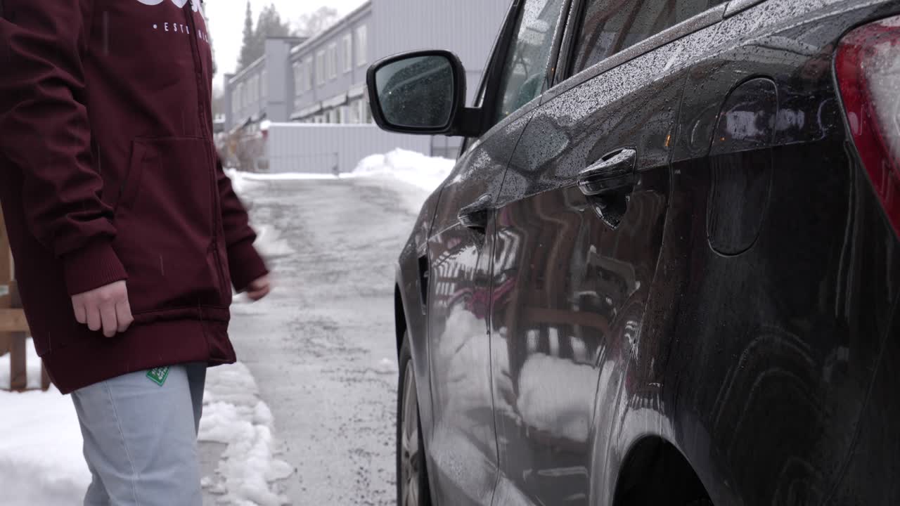 woman closing left car door of a black car in winter time, no face