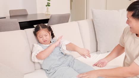 a father tends to his injured daughter on a sofa, providing care and comfort in a softly lit living room