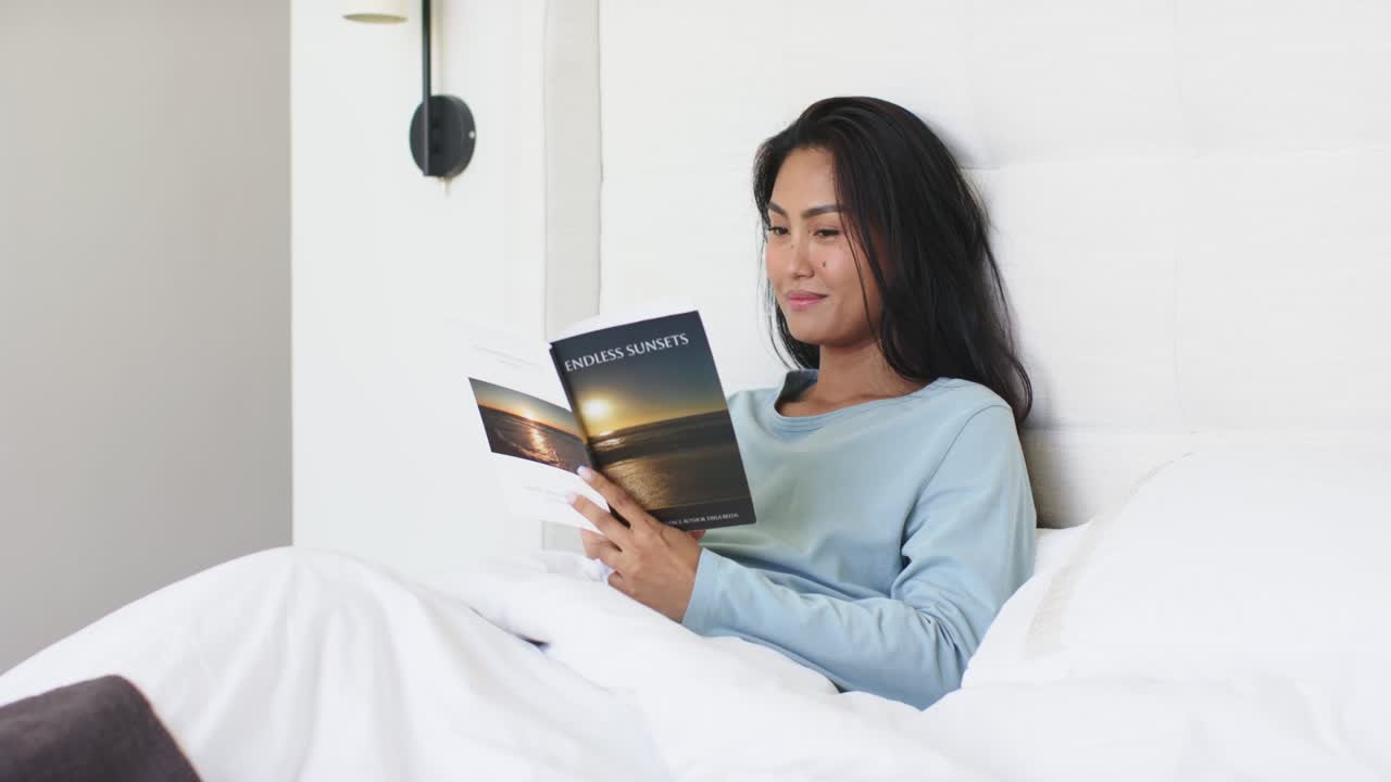 Catálogo com fotos de PÔR DO SOL SEM FIM: mulher asiática de meia-idade abrindo e examinando as páginas na cama com espaço para texto