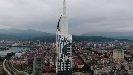 drone aerial view in georgia in batumi city around a skycreaper tower building with a small ferris wheel in it on a cloudy day next to the black sea and the beach