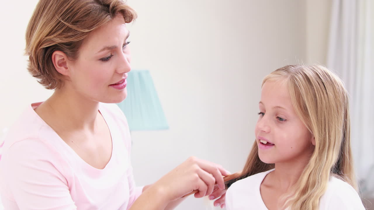 웃는 어머니가 딸의 머리카락을 고 있습니다.