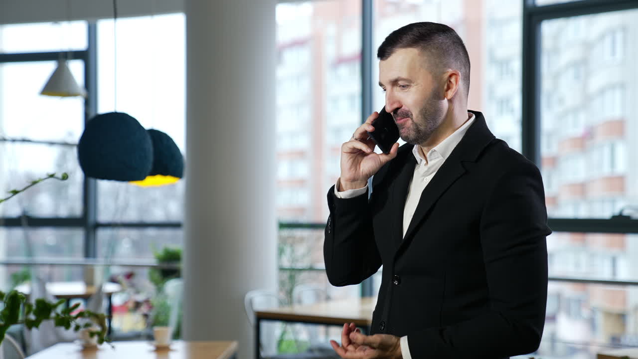 Businessman having a pleasant conversation on the mobile phone. Confident man has business talk on the phone. Big windows at the backdrop.