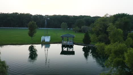 aerial shot of ripples in small pond with paddle board in center of pond and gazebo [4k