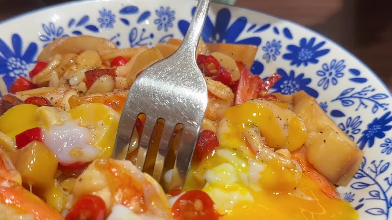 Una forchetta di metallo solleva un gamberetto cotto da una ciotola di riso piena di colori con tuorlo d'uovo che cola