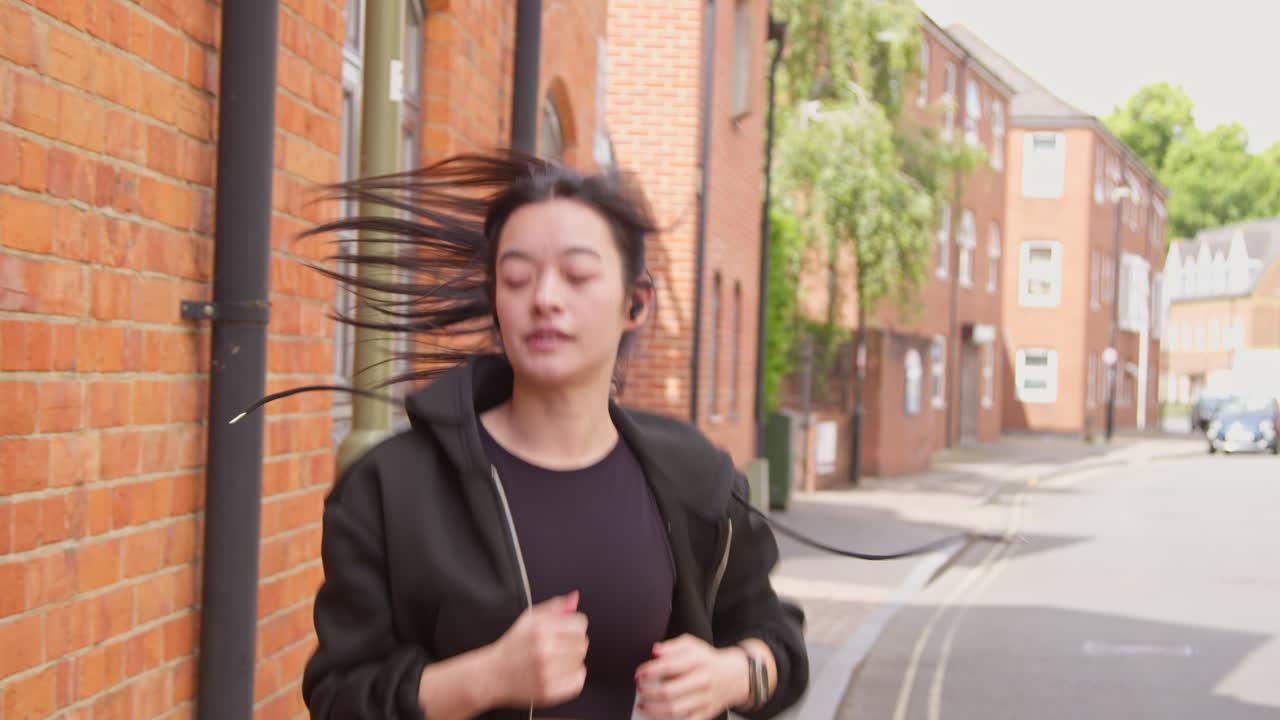 무선 이어폰과 스마트 시계를 착용하여 도시 거리를 따라 달리는 운동을 하는 젊은 여성