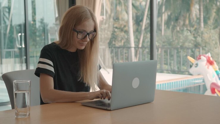 Young Woman in Glasses Typing on Laptop by a Swimming Pool