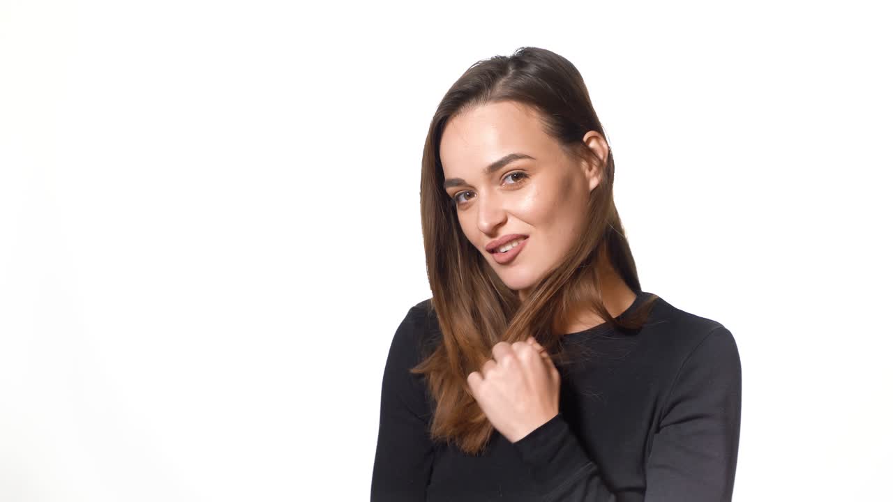A sexy girl in black golf is posing and tidying one's her hair on a white background in the studio.