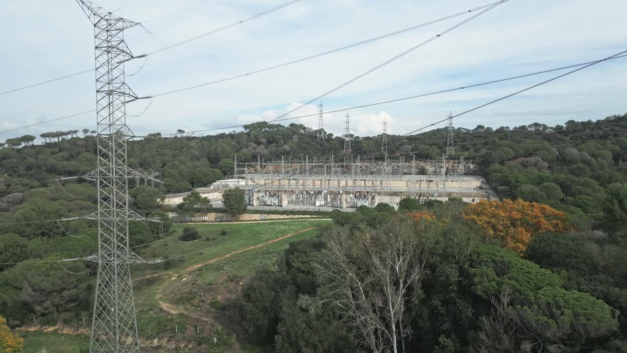 Power grid infrastructure nestled within verdant forest, showcasing intricate electrical substation surrounded by lush green trees and high voltage transmission lines, orbital drone shot